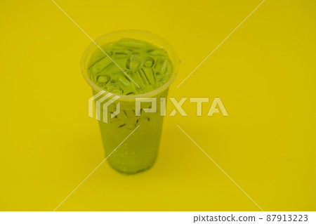 Green tea latte with ice in plastic cup and straw on yellow background. Homemade Iced Matcha Latte Tea with Milk take away Green tea latte with ice in plastic cup and straw on yellow background. Homemade Iced Matcha Latte Tea with Milk take away 87913223