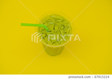 Green tea latte with ice in plastic cup and straw on yellow background. Homemade Iced Matcha Latte Tea with Milk take away Green tea latte with ice in plastic cup and straw on yellow background. Homemade Iced Matcha Latte Tea with Milk take away 87913224