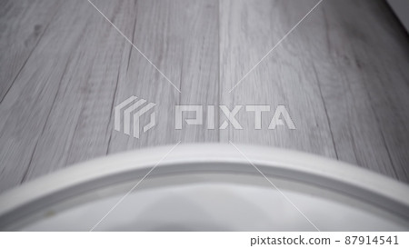 A white robot vacuum cleaner rides on a white parquet floor and collides with a human foot. The robot with artificial intelligence determines the space and cleans the floor. first-person view. 87914541