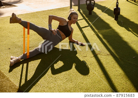 Cheerful woman training with elastic band outdoors 87915683