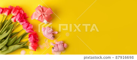 Pair of small baby girl socks, bouquet of pink tulips and gift box on yellow background with copy space for your warm message, baby shower, first newborn party background, copy space Pair of small baby girl socks, bouquet of pink tulips and gift box on yellow background with copy space for your warm message, baby shower, first newborn party background, copy space 87916698