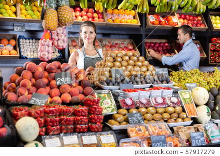 Portrait of welcoming female shop assistant and working male seller in fruit shop Portrait of welcoming female shop assistant and working male seller in fruit shop 87917279