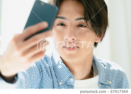 一個年輕人在他的智能手機上檢查他的髮型 87917369