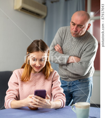 Jealous husband looking at his wife using smartphone 87917643