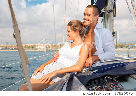 Young woman and man sitting on modern yacht deck, enjoying warm summer day during romantic sea travel Young woman and man sitting on modern yacht deck, enjoying warm summer day during romantic sea travel 87920079