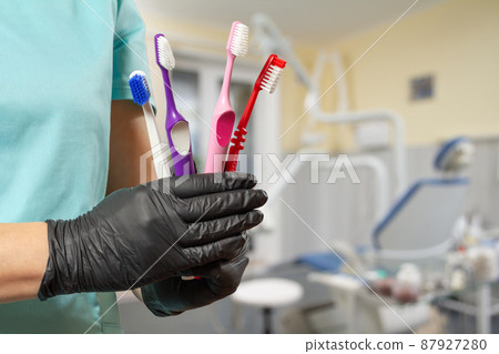 Dentist's hand in protective glove with toothbrushes. Dentist's hand in protective glove with toothbrushes. 87927280