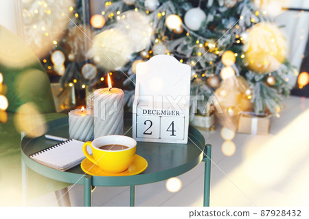 December 24 on wooden calendar standing on small table with burning candles in living room, selective focus. Christmas and New Year concept 87928432