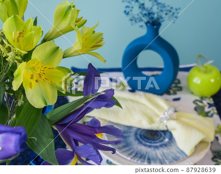 Table setting in blue and yellow colors. On a dark tablecloth a plate, a vase of flowers and decor Table setting in blue and yellow colors. On a dark tablecloth a plate, a vase of flowers and decor 87928639