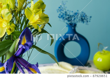 Table setting in blue and yellow colors. On a dark tablecloth a plate, a vase of flowers and decor 87928651