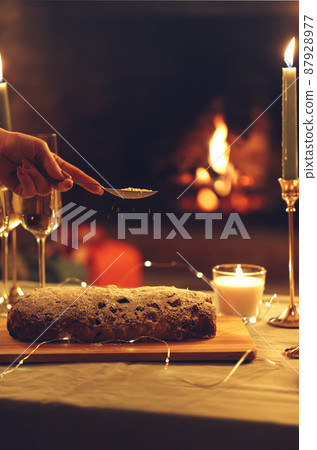 Christmas dinner. Female hand sprinkling sugar powder on xmas pie cake standing on rustic wooden table with glasses of champagne and burning candles Christmas dinner. Female hand sprinkling sugar powder on xmas pie cake standing on rustic wooden table with glasses of champagne and burning candles 87928977