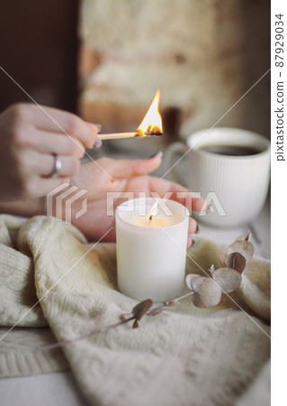 Cropped photo of female hands with lit match lighting candle on windowsill, hygge lifestyle Cropped photo of female hands with lit match lighting candle on windowsill, hygge lifestyle 87929034