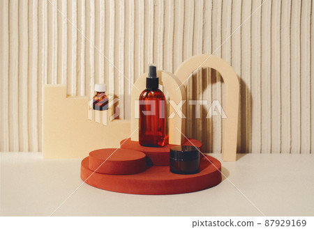Abstract composition with cosmetic skincare products in glass bottles standing on round podium against texture beige background, copy space for text. 87929169