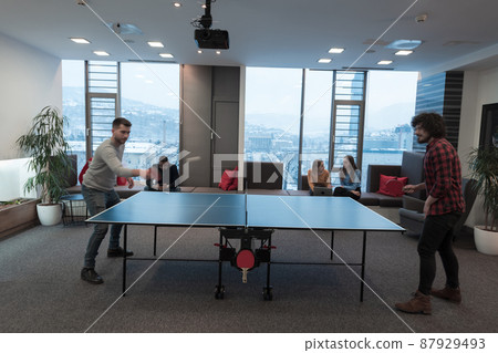 Two young start up business man playing ping pong tennis at modern creative office space people group have meeting and brainstorming in background Two young start up business man playing ping pong tennis at modern creative office space people group have meeting and brainstorming in background 87929493