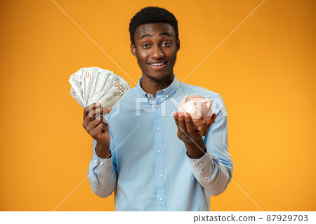 Young african amercian man holding piggy bank over yellow background Young african amercian man holding piggy bank over yellow background 87929703