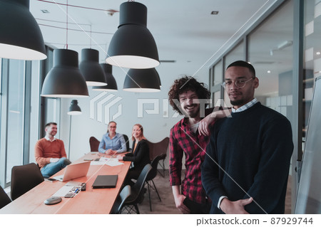 Portrait of two happy millennial male business owner in modern office. Two businessman smiling and looking at camera. Busy diverse team working in background. Leadership concept. Head shot. Portrait of two happy millennial male business owner in modern office. Two businessman smiling and looking at camera. Busy diverse team working in background. Leadership concept. Head shot. 87929744