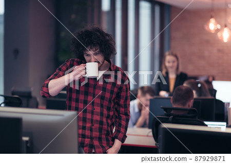 Smiling businessman in afro shirt standing in modern office with cup of coffee in hand. Selective focus  87929871