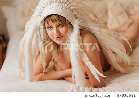 a topless happy blonde woman in an Indian headdress of white feathers in bed a topless happy blonde woman in an Indian headdress of white feathers in bed 87930681