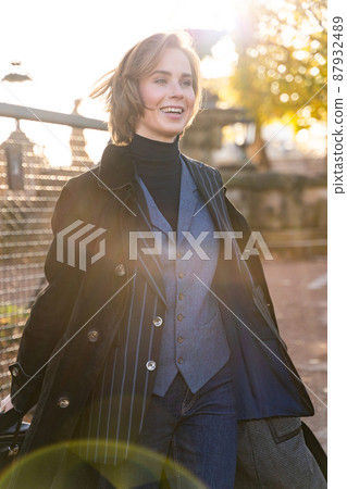 Young blond short-haired woman in striped jacket, jeans and vest touches hair Young blond short-haired woman in striped jacket, jeans and vest touches hair 87932489