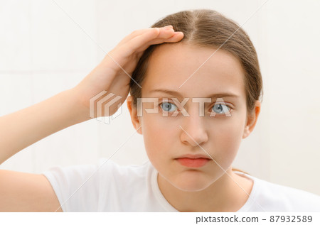 the face of a teenage girl, she looks at herself in the mirror and touches her face with her hand, good and clean skin is a concept of beauty and health the face of a teenage girl, she looks at herself in the mirror and touches her face with her hand, good and clean skin is a concept of beauty and health 87932589