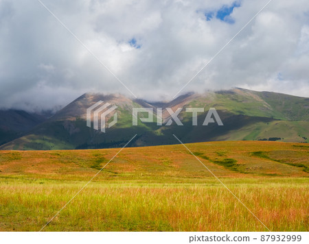 Sun after the rain over the summer mountain plateau. Dramatic rainy alpine landscape in green valley and dark mountain sharps in low clouds. Atmospheric awesome view to pointy mountain in low clouds. 87932999