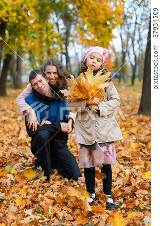 Portrait of a family in an autumn park. Happy parents and unhappy child posing with yellow leaves. Portrait of a family in an autumn park. Happy parents and unhappy child posing with yellow leaves. 87934509