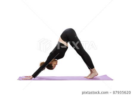 Portrait of young woman in black gym clothes training on purple yoga mat isolated over white studio background 87935620
