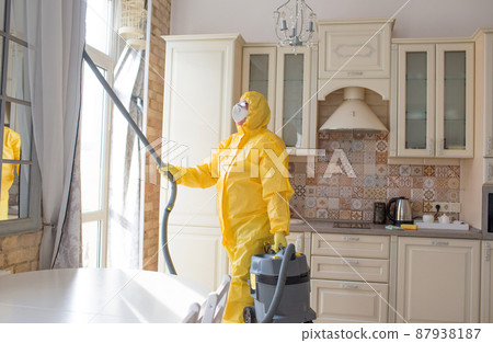 a man in a protective suit cleans the room with a vacuum cleaner. 87938187