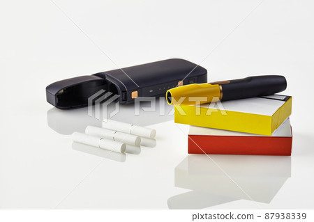 Black electronic cigarette is on packs with red and yellow sides, open battery, three heatsticks isolated on white. Heating tobacco system. Close up 87938339