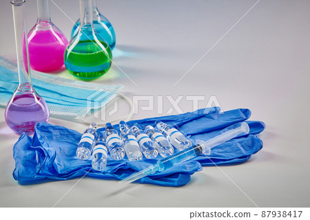 Medical flasks with colorful chemical reagents. Seven mockup ampoules and syringe on blue disposable gloves, mask isolated on white. Coronavirus 87938417