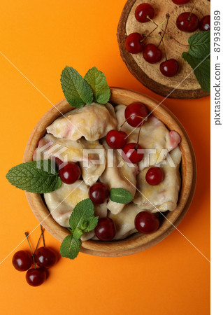 Wooden bowl with pierogi with cherry on orange background 87938989