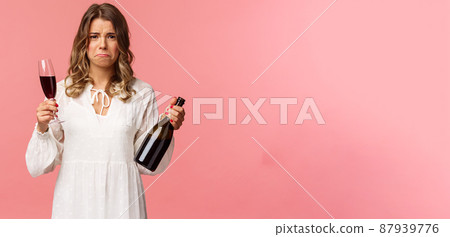 Holidays, spring and party concept. Portrait of upset and whining young blond woman being cheated trying to ease pain with alcohol, holding glass wine and bottle, grimacing want cry, complaining 87939776