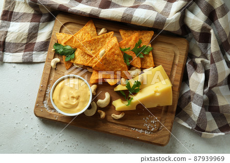 Board with cheese sauce and snacks on white textured table 87939969
