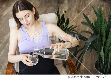 Hydration during pregnancy. Young pregnanat woman in t-shirt sitting on bed at home, drinking clean mineral water Hydration during pregnancy. Young pregnanat woman in t-shirt sitting on bed at home, drinking clean mineral water 87941760