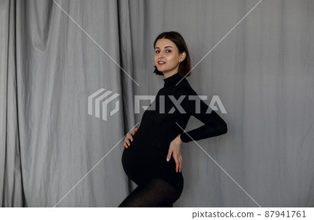 Pregnant woman standing against gray background wearing black clothes Pregnant woman standing against gray background wearing black clothes 87941761