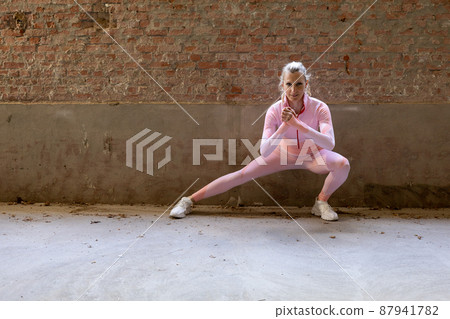 Beautiful young blonde fitness woman wearing pink sports clothes stretching and warming up legs in Beautiful young blonde fitness woman wearing pink sports clothes stretching and warming up legs in 87941782