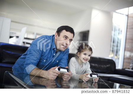 Smiling young man playing videogame together with daughter in modern living room Smiling young man playing videogame together with daughter in modern living room 87941832