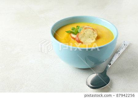 Plate of pumpkin soup and spoon on white textured table 87942256