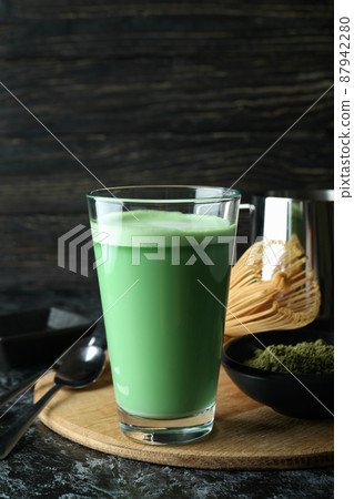 Glass of matcha latte and accessories for making on black smokey table 87942280
