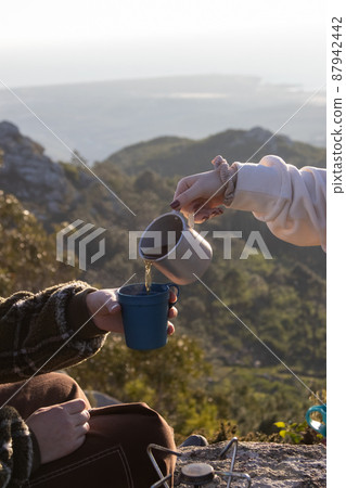 Woman pouring hot tea in cup of her girlfriend outdoors 87942442