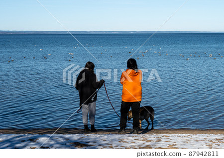 A mother and daughter at a winter beach covered with snow and a blue sky in the background A mother and daughter at a winter beach covered with snow and a blue sky in the background 87942811