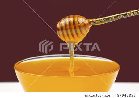 fresh fragrant honey drips from a spoon into a plate on a colored background.  87942855