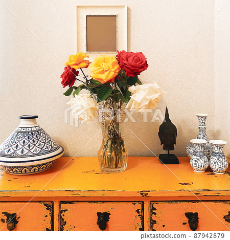 Bouquet of fresh multicolored rose flowers in glass vase on yellow vintage table with buddha head 87942879