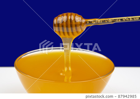 fresh fragrant honey drips from a spoon into a plate on a colored background. fresh fragrant honey drips from a spoon into a plate on a colored background. 87942985