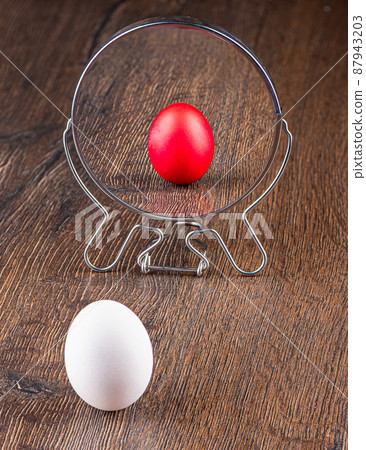 A white chicken egg on a wooden background is reflected in the mirror like an Easter colored egg. A white chicken egg on a wooden background is reflected in the mirror like an Easter colored egg. 87943203