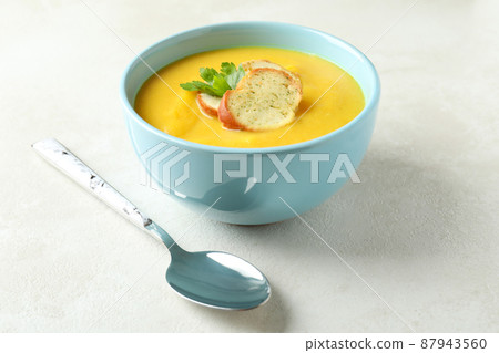 Plate of pumpkin soup and spoon on white textured table 87943560