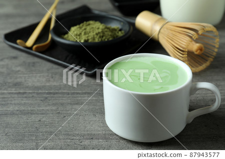 Cup of matcha latte and accessories for making on gray textured table Cup of matcha latte and accessories for making on gray textured table 87943577