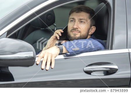 Successful business man with a phone in his hand sits behind the wheel of a prestigious car Successful business man with a phone in his hand sits behind the wheel of a prestigious car 87943899