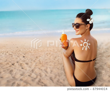Skin care. Sun protection. Woman apply sun cream. Woman With Suntan Lotion On Beach In Form Of The Sun. Portrait Of Female With Drawn Sun On A Shoulder. Suncream. Girl Holding Moisturizing Sunblock. Skin care. Sun protection. Woman apply sun cream. Woman With Suntan Lotion On Beach In Form Of The Sun. Portrait Of Female With Drawn Sun On A Shoulder. Suncream. Girl Holding Moisturizing Sunblock. 87944014