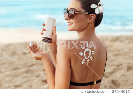 Facial Care. Young Female Holding Bottle Sun Cream and Applying on Face Smiling. Beauty Face. Portrait Of Young Woman in hat Smear Moisturizing Lotion on Skin. SkinCare Facial Care. Young Female Holding Bottle Sun Cream and Applying on Face Smiling. Beauty Face. Portrait Of Young Woman in hat Smear Moisturizing Lotion on Skin. SkinCare 87944015