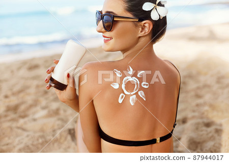 Woman Applying Sun Cream  on Tanned  Shoulder In Form Of The Sun. Sun Protection.Sun Cream. Skin and Body Care. Girl Using Sunscreen to Skin. Female Holding Suntan Lotion and Moisturizing Sunblock. 87944017